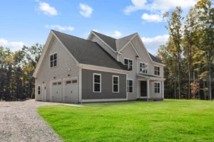 A two-story gray house with white trim and a double garage, set on a grassy lawn and surrounded by trees under a blue sky.