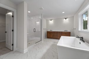 Spacious bathroom with a glass-enclosed shower, double sink vanity with wooden cabinetry, bathtub, and closet. White walls and marble flooring create a clean, modern look.