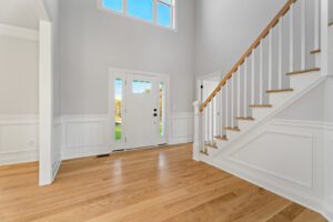 Bright entryway featuring a white front door with windows, wooden stairs with white risers and balusters, and hardwood floors.