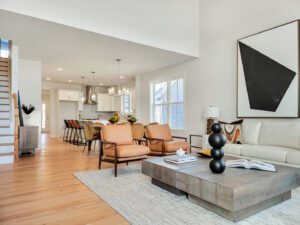 A modern, open-concept living and dining area featuring neutral tones, leather chairs, a large abstract painting, and a kitchen with an island and barstools.