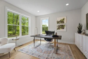 A modern home office on Vista View Dr features a desk, chair, large window, and plants, offering a breathtaking overlook of the lush green yard.