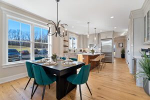 A modern kitchen and dining area with a large window, green chairs, a black dining table, an island with bar stools, stainless steel appliances, and hardwood floors.