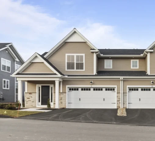 Modern duplex at 51 Soderman Way, with beige siding, white garage doors, and a paved driveway under a blue sky.