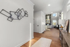 Modern hallway with abstract wall art, light hardwood floor, Summertime Circle rug, and view into a living room with stone fireplace.