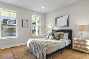 A modern bedroom in Summertime Circle, with a large bed, fluffy throw, nightstand lamps, and a window inviting natural light.