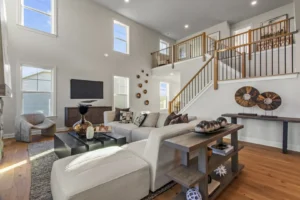 Modern living room with white sectional sofa, Summertime Circle wall decor, TV, and staircase to upper floor with wooden railing.