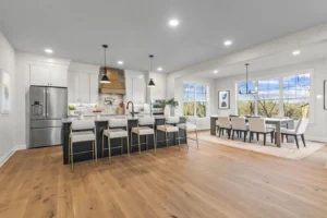 Spacious kitchen and dining area with wood flooring, a large island, modern appliances, and large windows perfect for summertime.