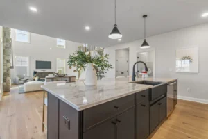 Modern open-concept kitchen on Summertime Circle with a marble island, pendant lights, and a view of the living rooms stone fireplace.