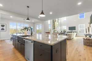 Modern open-plan kitchen and living area with island, circle pendant lights, summertime windows, and a high ceiling.