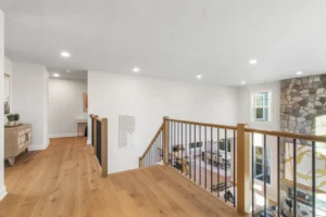 Bright modern hallway on Summertime Circle features wooden floors, a metal and wood railing, and a view of the stone fireplace.