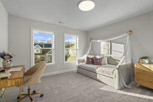 Bright bedroom with a daybed, canopy, and two windows. A Summertime Circle desk with floral arrangement is on the left.