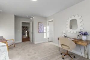 Bright home office with beige carpet, wooden desk, white chair, mirror, Summertime Circle artwork, and doorway to hallway.