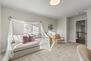 Bright bedroom with a daybed, purple cushions, soft lighting, circle wall decor, and a wooden chair on carpeted floor.