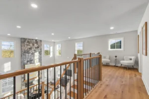 Bright loft area with stone fireplace, modern chairs in a circle, and hardwood floors overlooking a spacious living room.