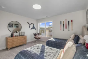 Bright bedroom with two beds, sports decor, Summertime Circle mirror above dresser, and teddy bear in chair by window.