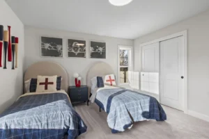 Two twin beds with blue plaid bedding in the Summertime Circle bedroom, adorned with wall art and a small nightstand.