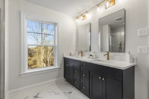 Modern bathroom with dual sinks, gold faucets, and large mirrors overlooking Summertime Circles lush trees. Marble floor tiles.