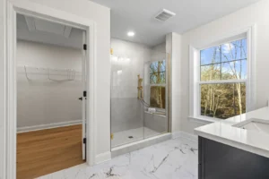 Summertime Circle bathroom with glass shower, white walls, marble floor, tree views, and adjacent walk-in closet.