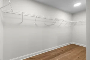 Summertime glow fills the walk-in closet with white wire shelving and a polished circle of hardwood floor.