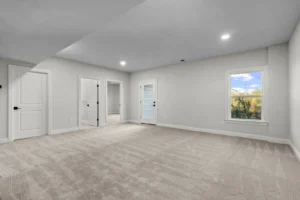 A serene carpeted room with white walls, two open doors, a window framing Summertime Circles trees, and recessed lighting.