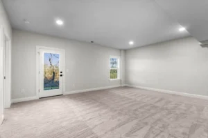 Empty room with beige carpet, white walls, and a glass door leading outside. Two windows let in Summertime Circles light.