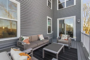 Modern outdoor patio in Summertime Circle with gray sectional sofas, accent pillows, a black rug, and a glass sliding door.