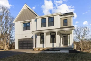 White two-story house with black accents, large garage, and grassy front yard under the summertime sky with clouds.