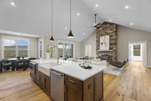 Spacious open-concept kitchen and living area with a large island, pendant lights, wood flooring, and a stone fireplace. A dog portrait hangs above the fireplace.