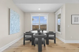 A modern dining room with a black table, six dark gray chairs, and large windows. Neutral walls feature abstract artwork, and light wood flooring adds warmth to the space.