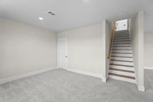 A carpeted room with beige walls and a closed door, featuring a staircase leading upward.