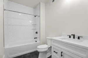 Modern bathroom with white subway tile bathtub, black fixtures, white vanity, and dark floor tiles.