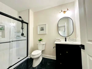 Modern bathroom with a glass-enclosed shower, black vanity with oval mirror, and a toilet. Black and white color scheme with marble floor.