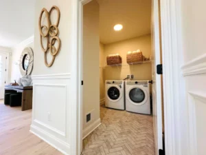 View of a laundry room with a washing machine and dryer, two baskets on a shelf above, and decorative wall art in the hallway.